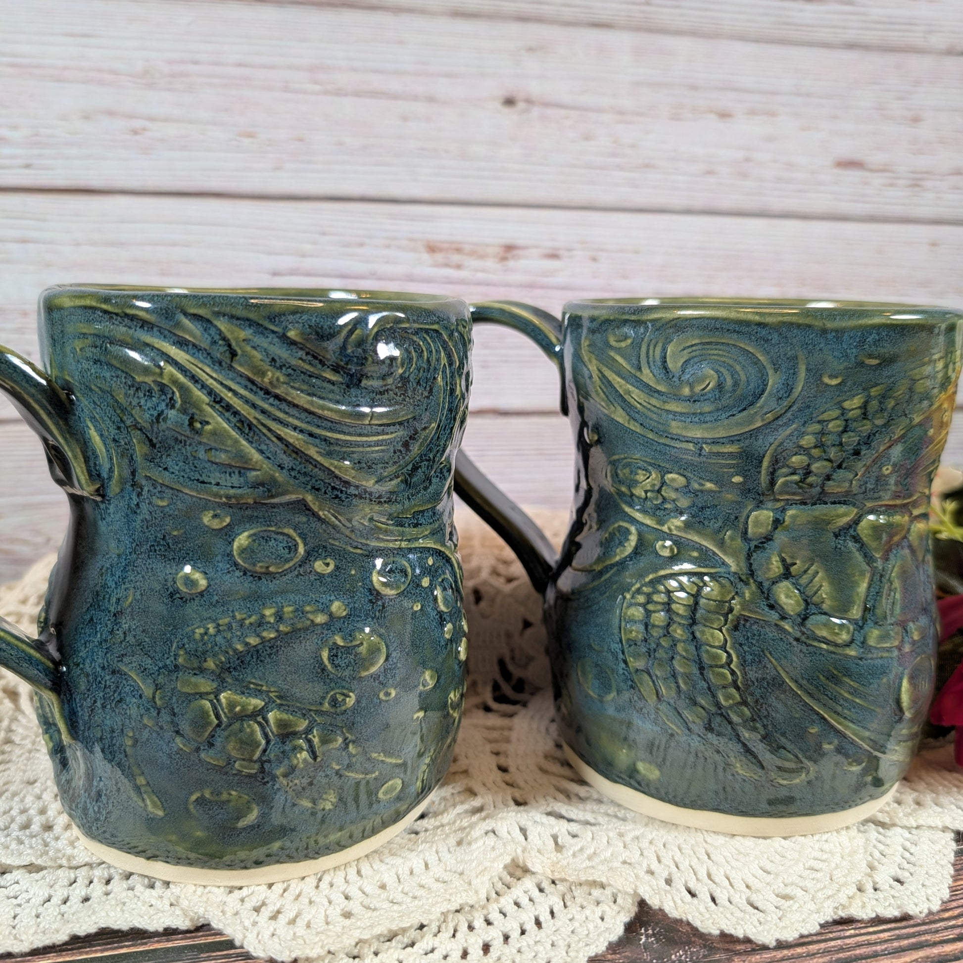Two green ceramic mugs with textured design on a white doily.