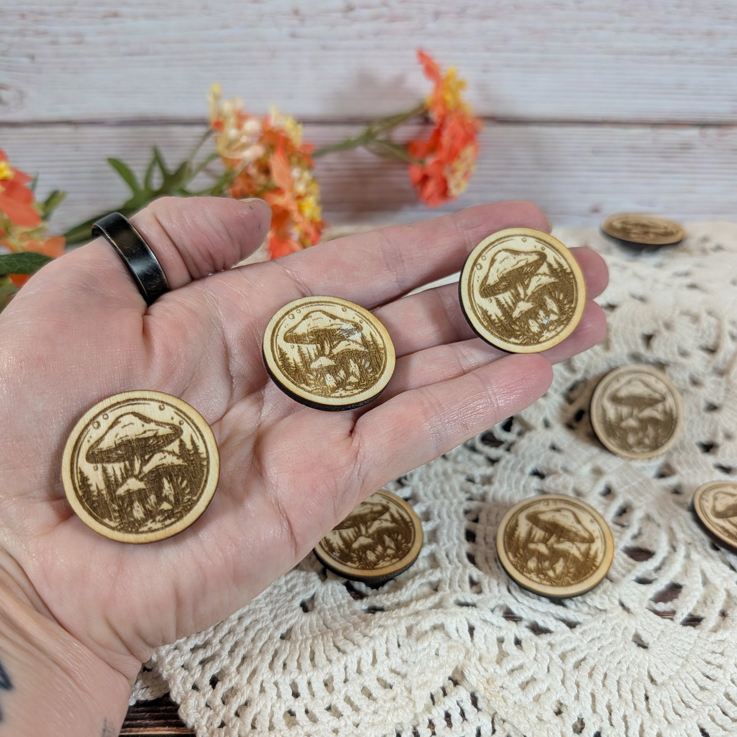 Hand holding round mushroom magnets with flowers in the background