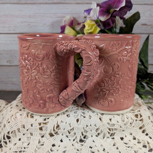 Two pink ceramic mugs with floral patterns on a lace tablecloth.
