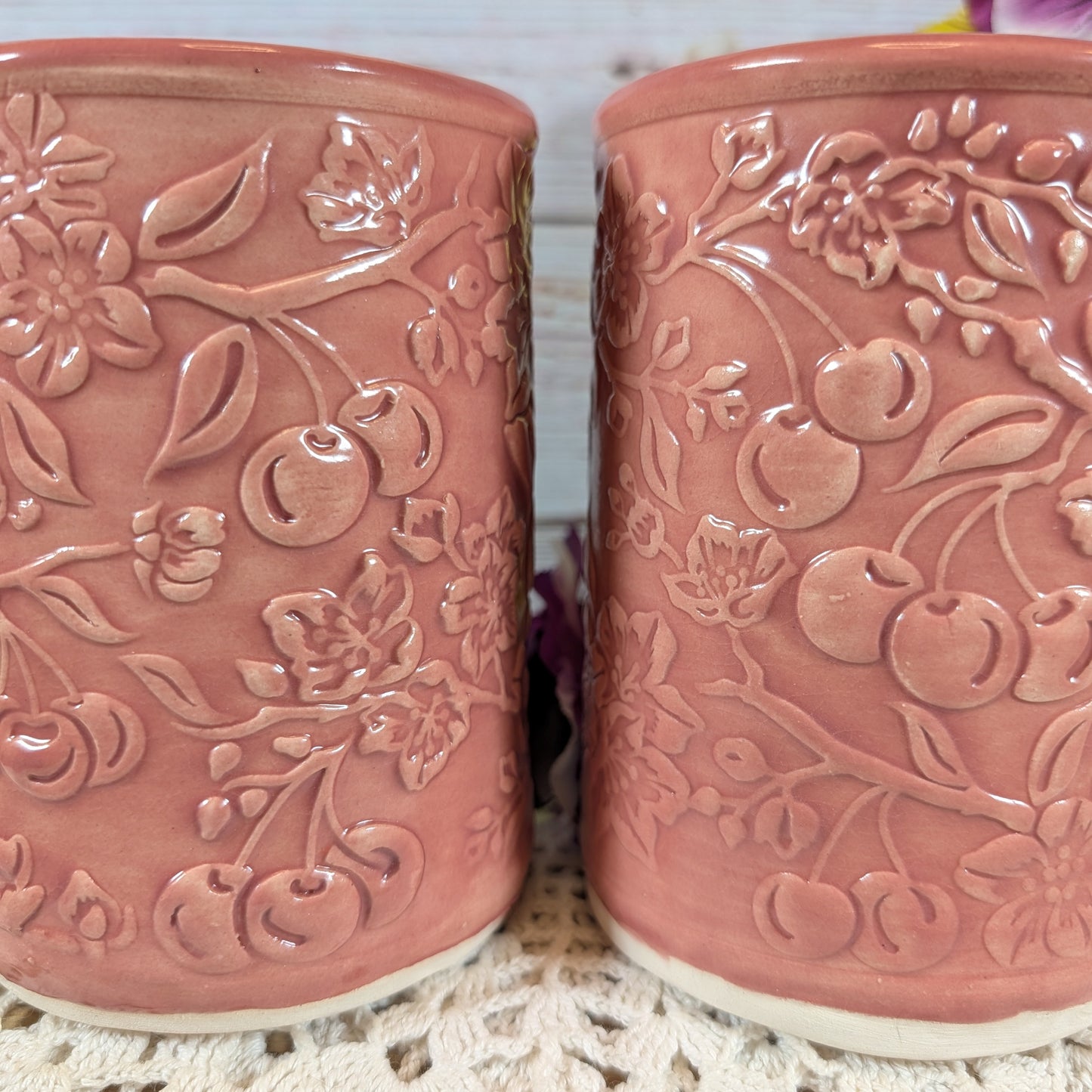 Two pink ceramic mugs with floral and cherry designs on a textured surface.
