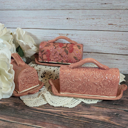 Three ceramic butter dishes with floral designs on a wooden surface.