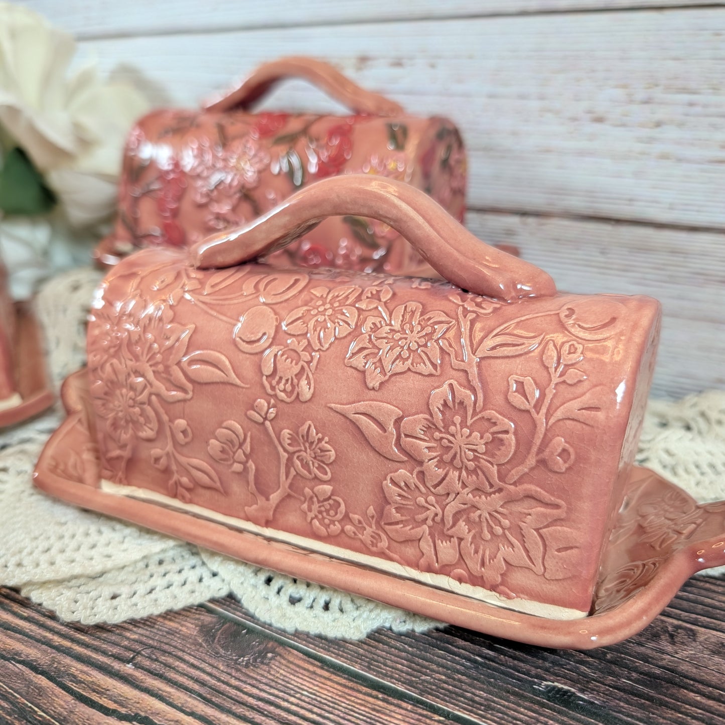 Pink ceramic butter dish with floral embossing on a wooden surface