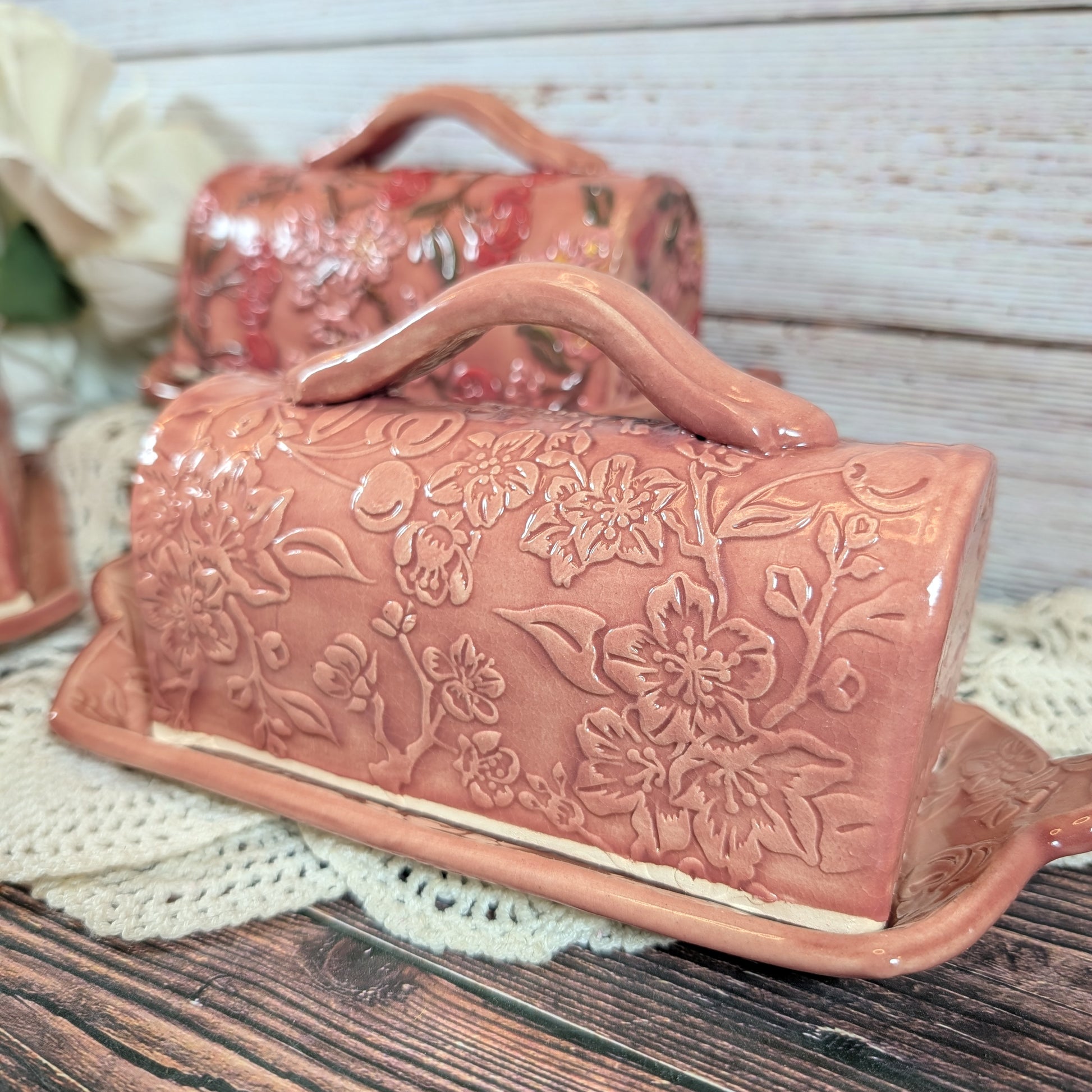 Pink ceramic butter dish with floral embossing on a wooden surface