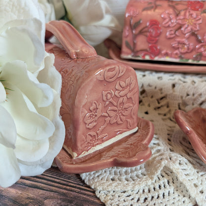 Pink ceramic butter dish with floral design on a lace tablecloth