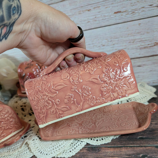 Ceramic butter dish with floral patterns held by a hand on a wooden surface