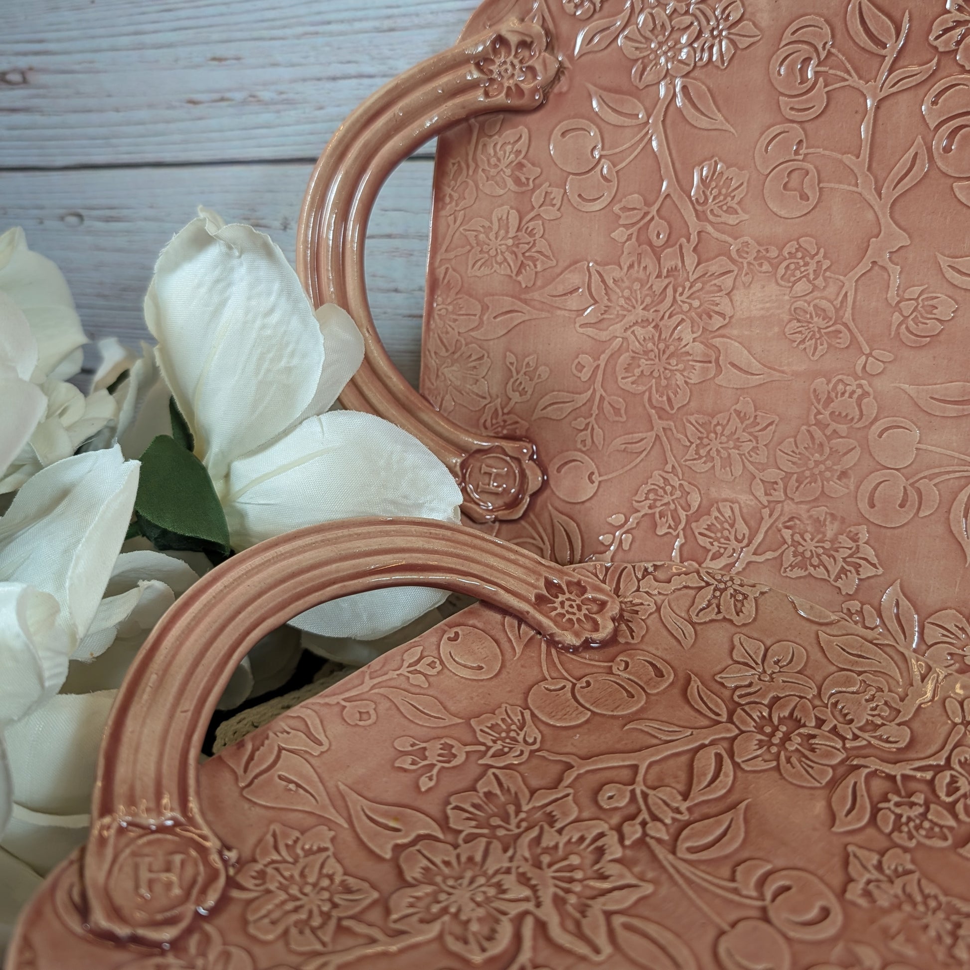 Closeup of the handles of two long pink trays with floral patterns on a wooden surface