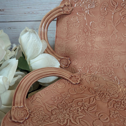 Closeup of the handles of two long pink trays with floral patterns on a wooden surface