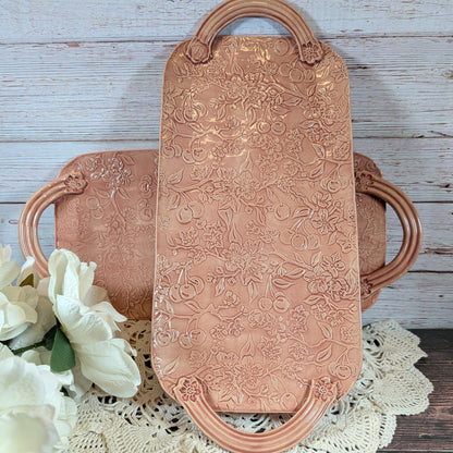 Two long pink trays with floral patterns on a wooden surface