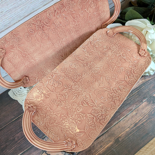 Two long pink trays with floral patterns on a wooden surface