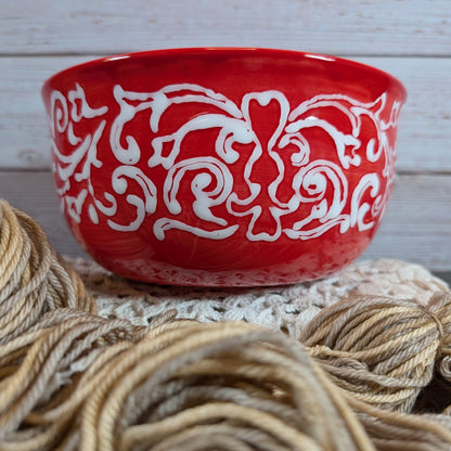 Red yarn bowl with white patterns on a wooden surface with yarn.