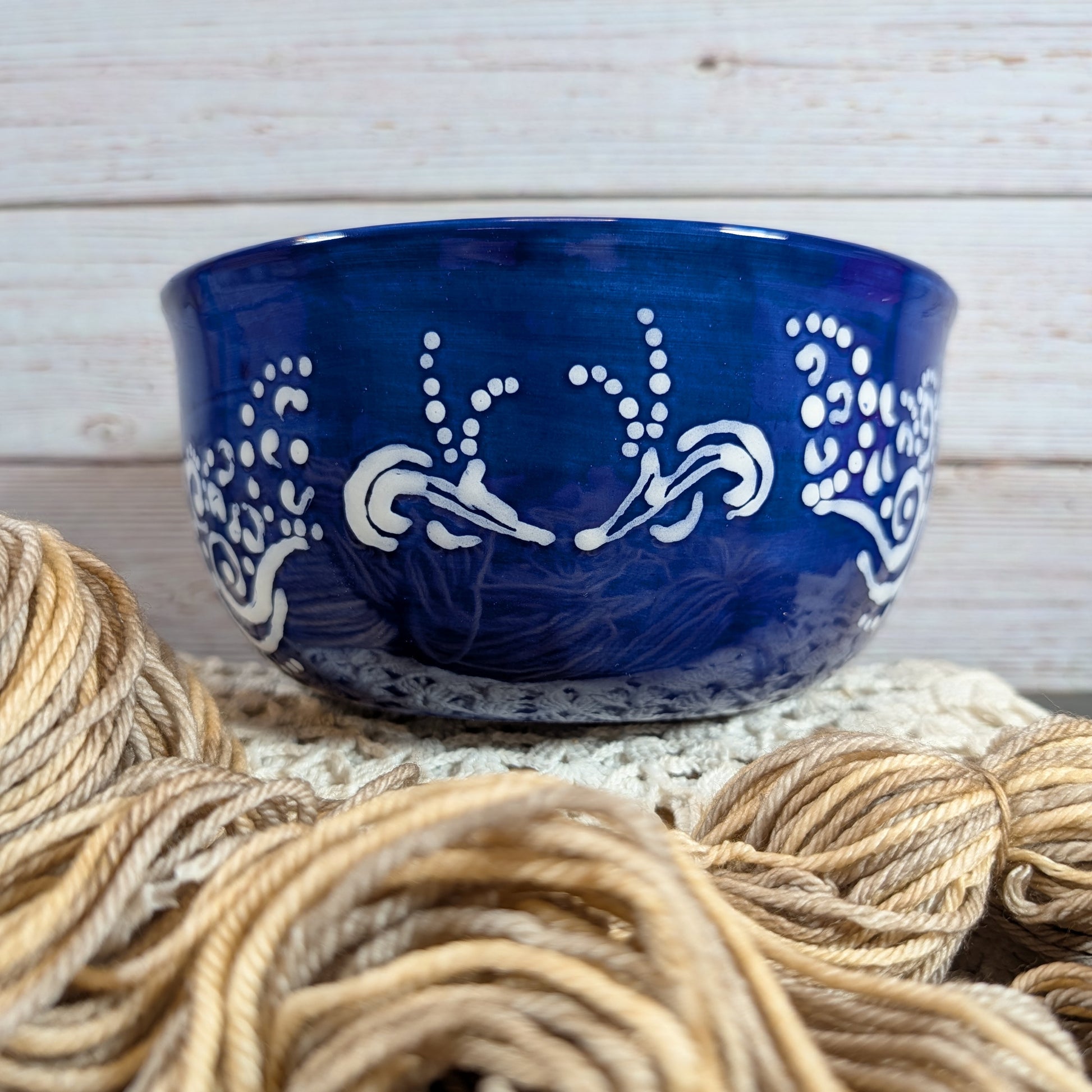 Blue ceramic yarn bowl with white patterns on a wooden surface with beige yarn.