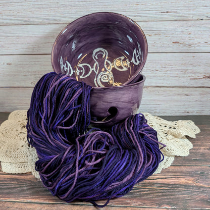 Purple yarn skein with a ceramic yarn bowl on a wooden surface