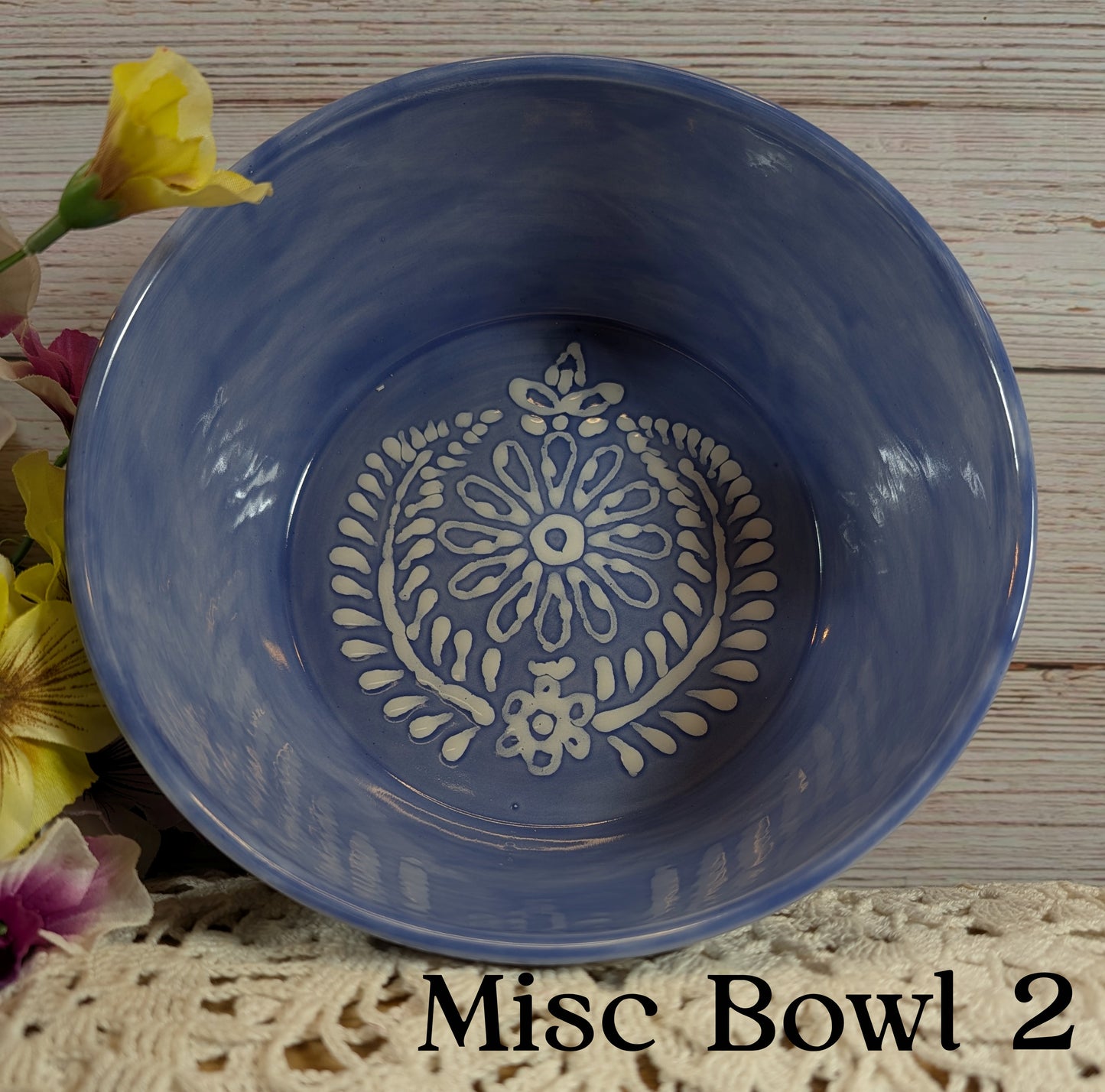 Blue ceramic bowl with decorative white pattern on a wooden surface with flowers.