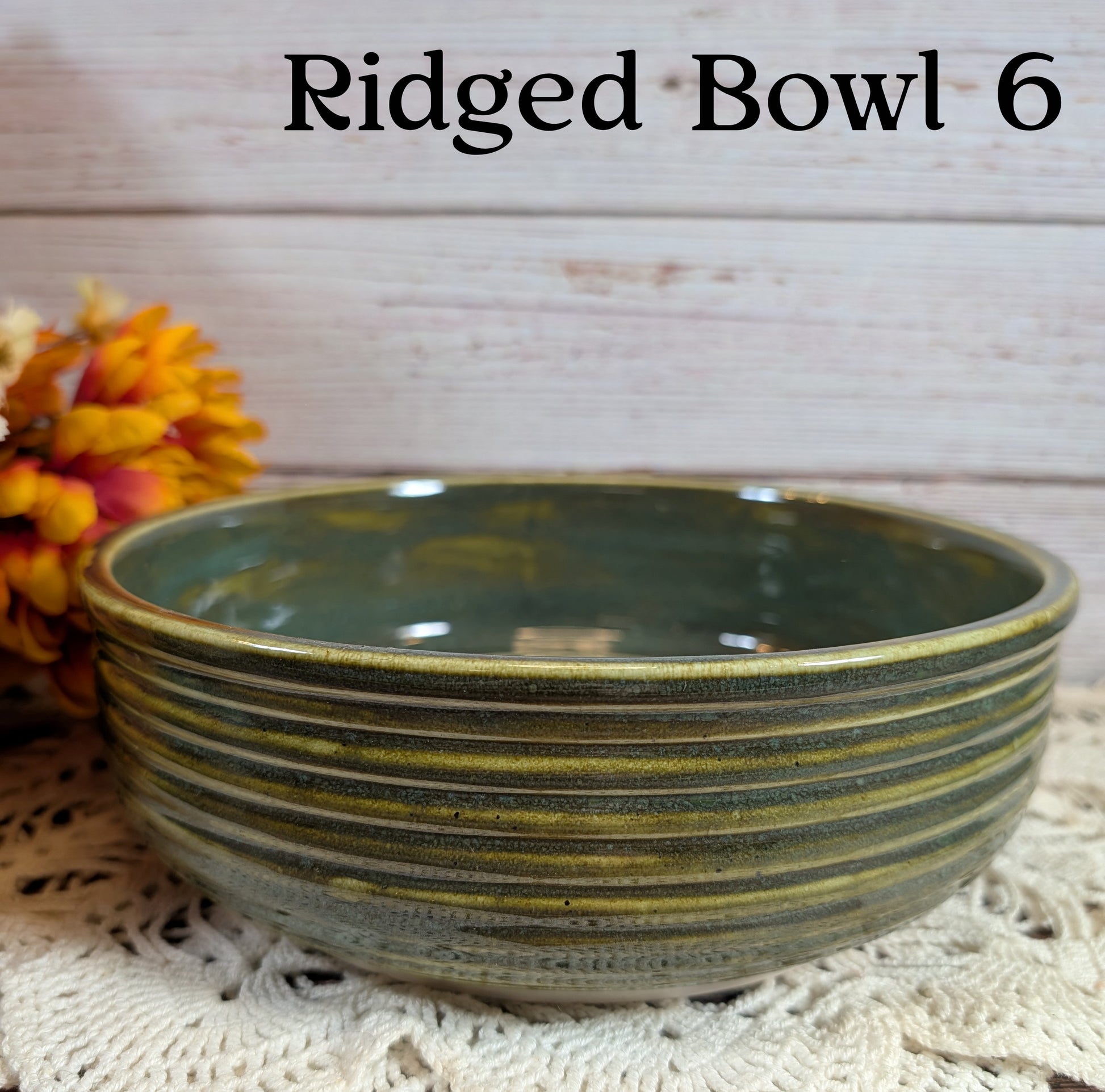 Green ridged bowl on a textured surface with flowers in the background
