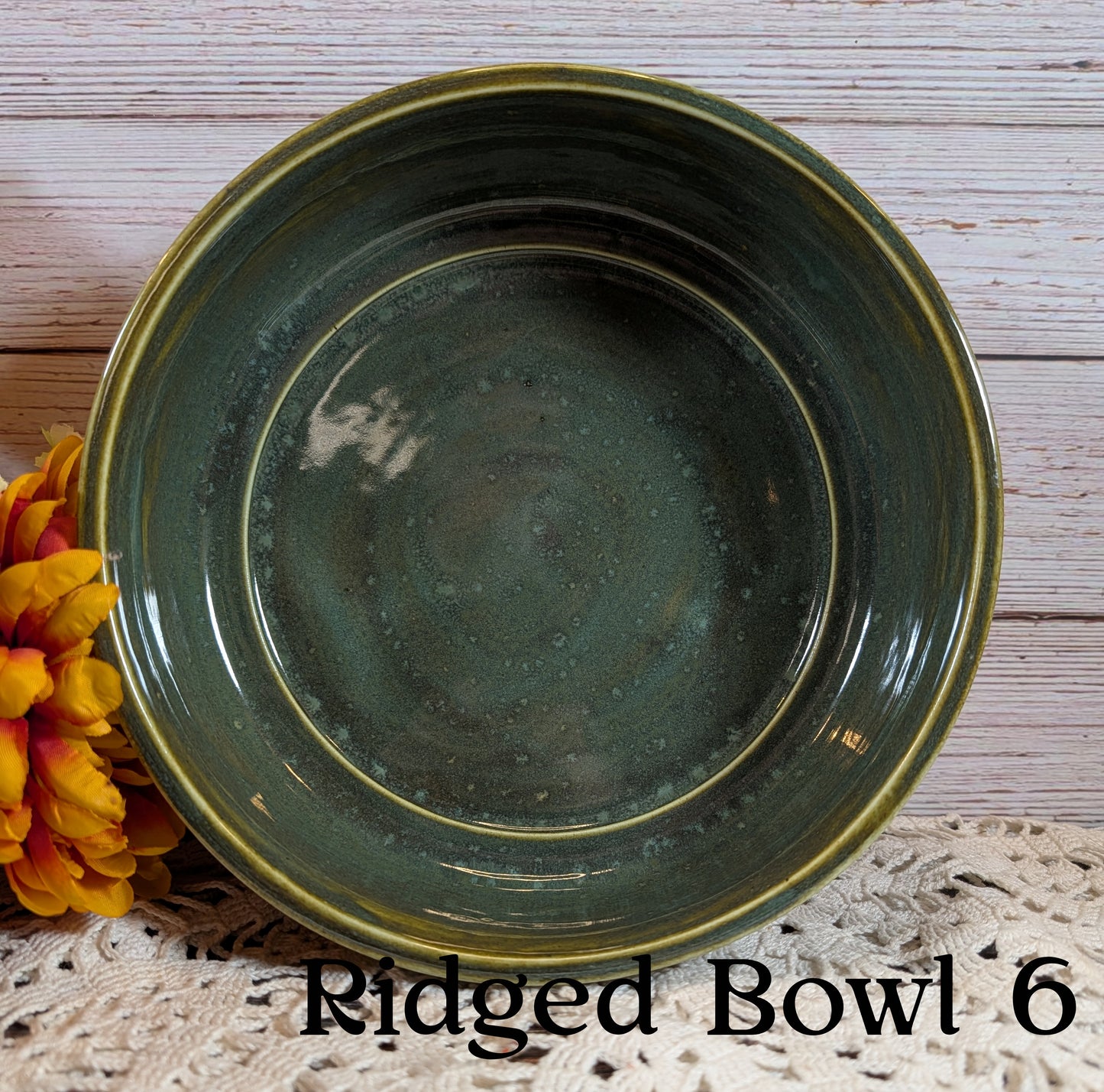 Green ridged bowl labeled 'Ridged Bowl 6' on a wooden surface with flowers.