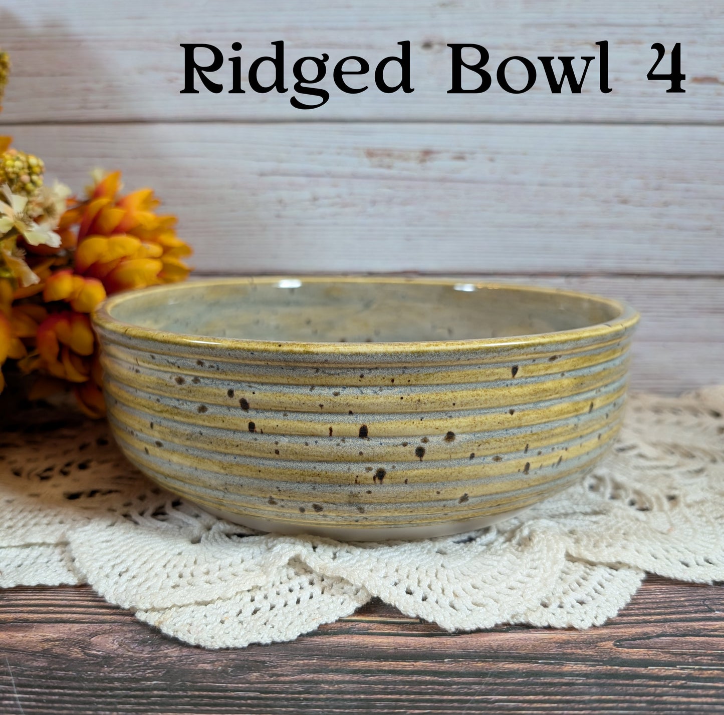 Ridged ceramic bowl, yellow and gray with black spots, on a lace doily with flowers in the background