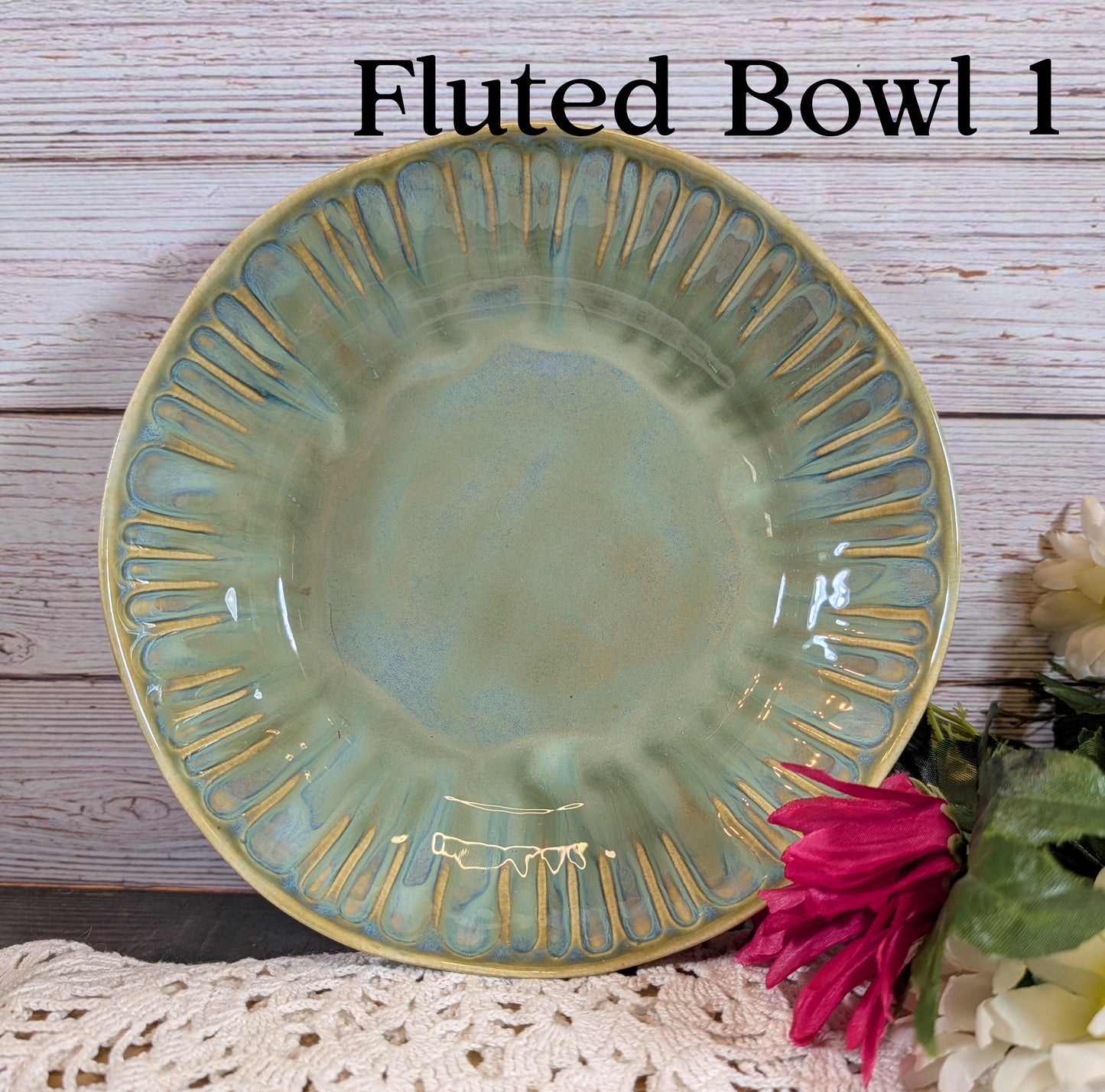 Green fluted bowl on a wooden surface with a pink flower