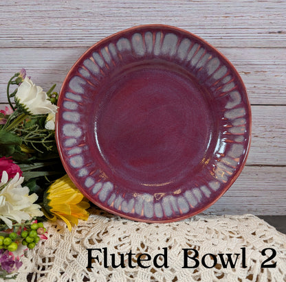 Purple fluted bowl on a wooden surface with flowers and lace