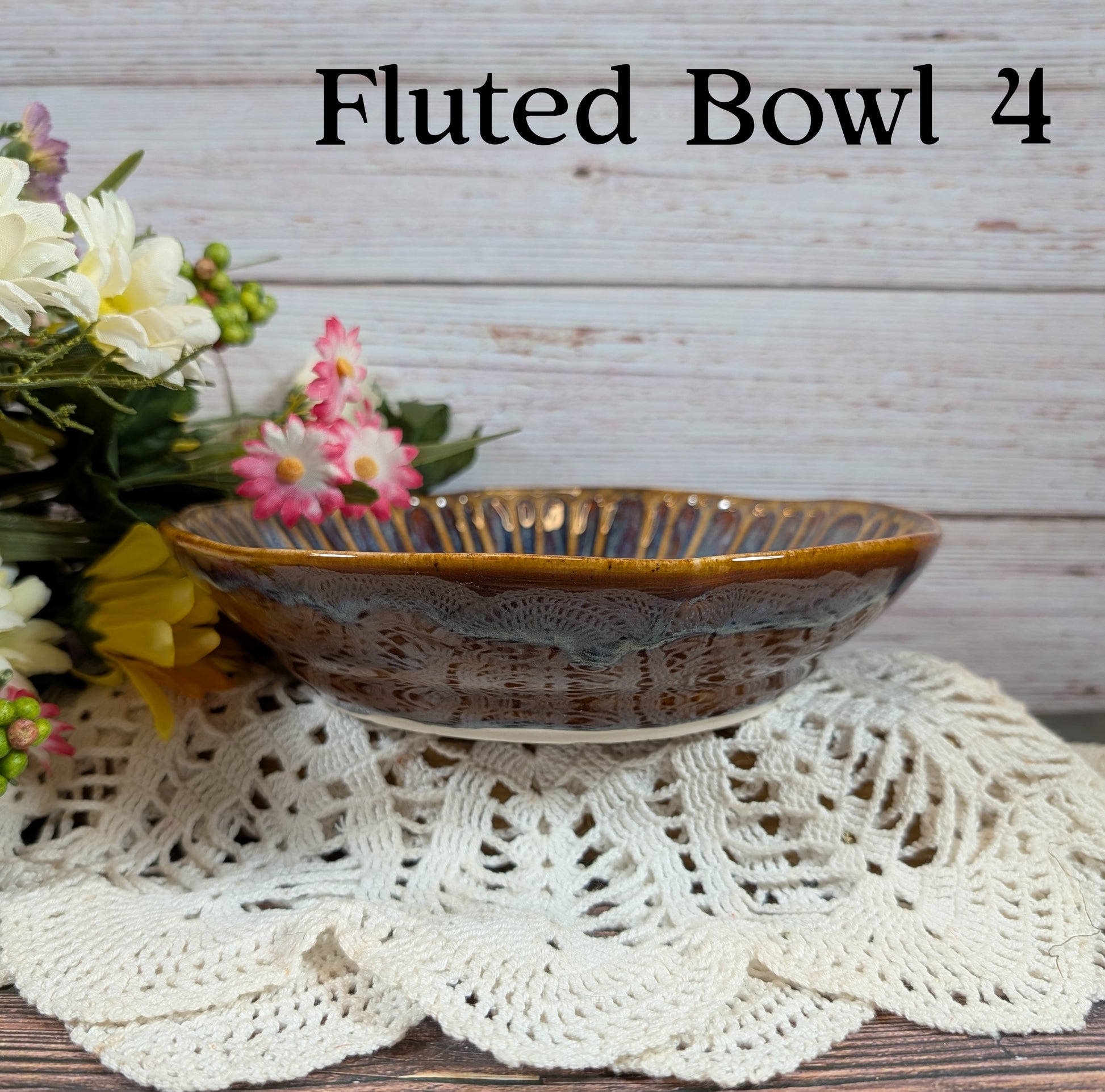 Brown and gold bowl on a lace doily with flowers in the background