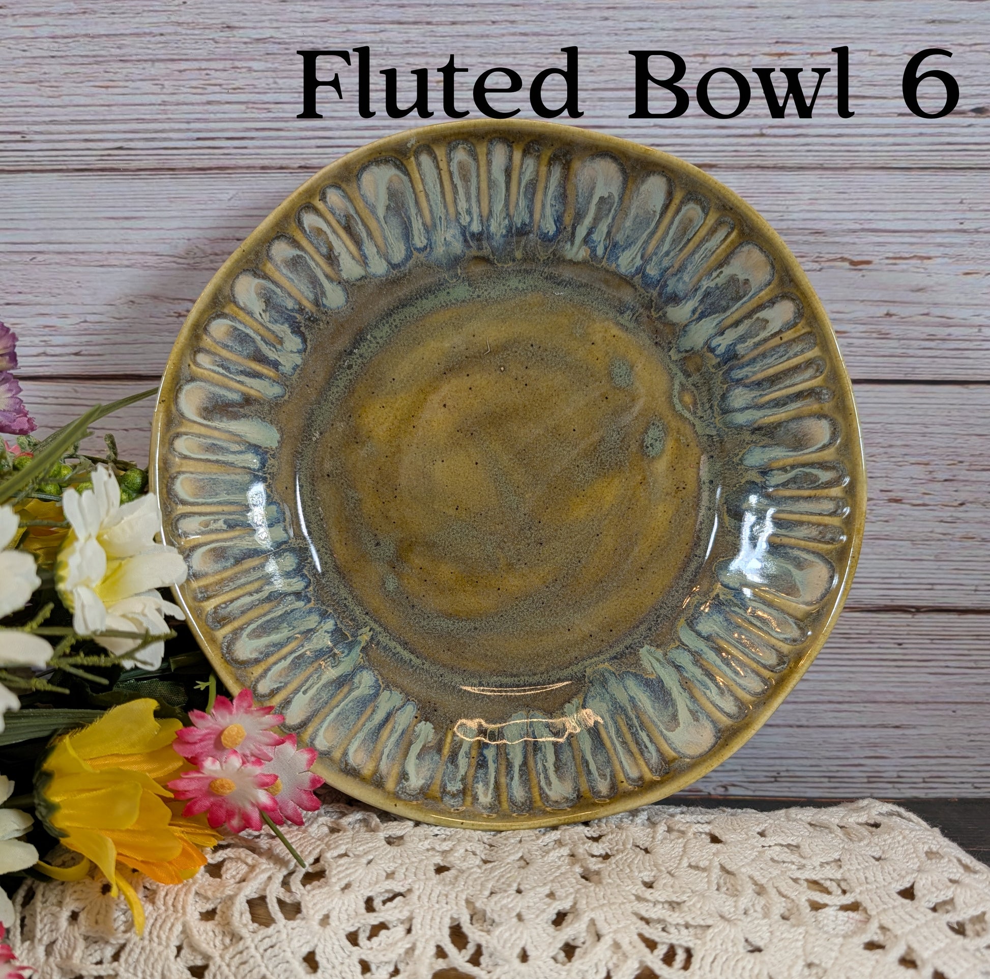 Green ceramic bowl with decorative edge on a wooden surface with flowers.