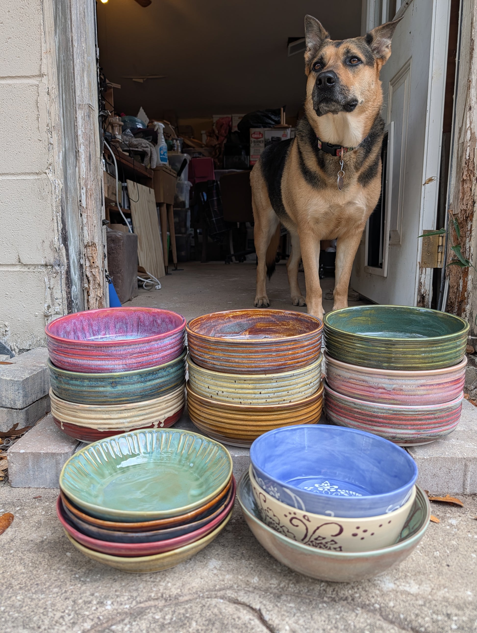 Stacks of colorful ceramic plates and bowls with a dog standing nearby.