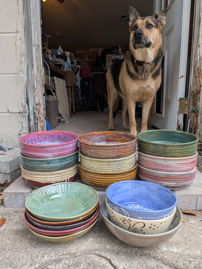 Stacks of colorful ceramic plates and bowls with a dog standing nearby.