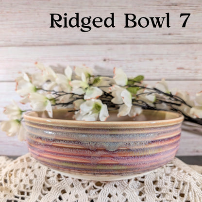 Pink, gray, and yellow ceramic bowl with floral arrangement on a textured surface