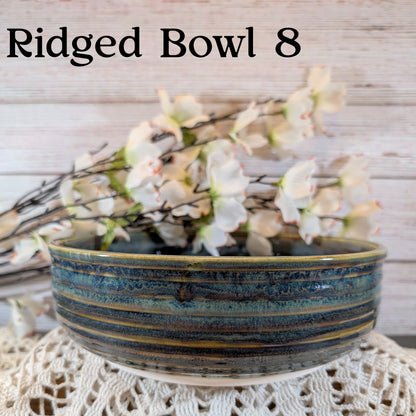 A multicolored blue and brown bowl with floral arrangement on a lace doily with a wooden background.
