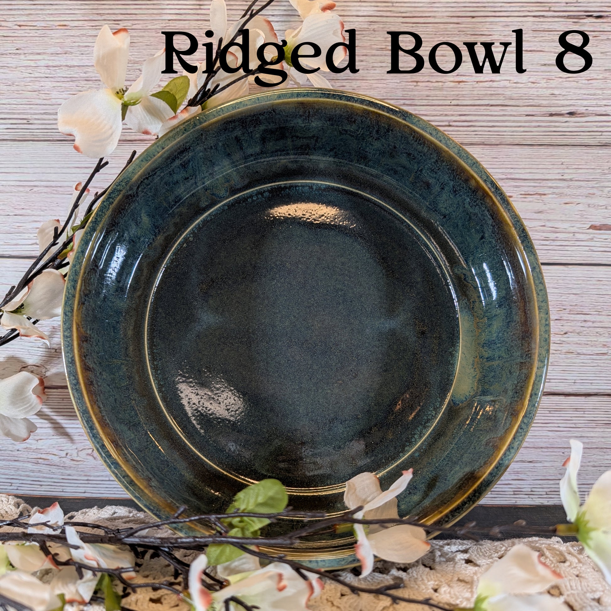 A multicolored blue and brown bowl with floral arrangement on a lace doily with a wooden background.