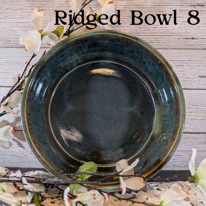 A multicolored blue and brown bowl with floral arrangement on a lace doily with a wooden background.