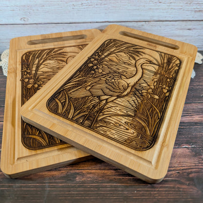 Two wooden charcuterie boards with engraved designs of a bird and nature on a wooden surface.