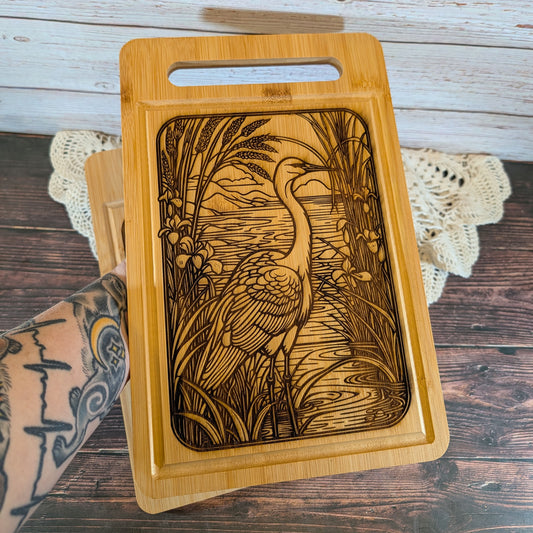 Wooden cutting board with engraved design of a crane and landscape on a wooden surface.