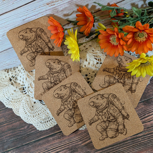 Set of cork coasters with capybara illustrations on a wooden surface with flowers.