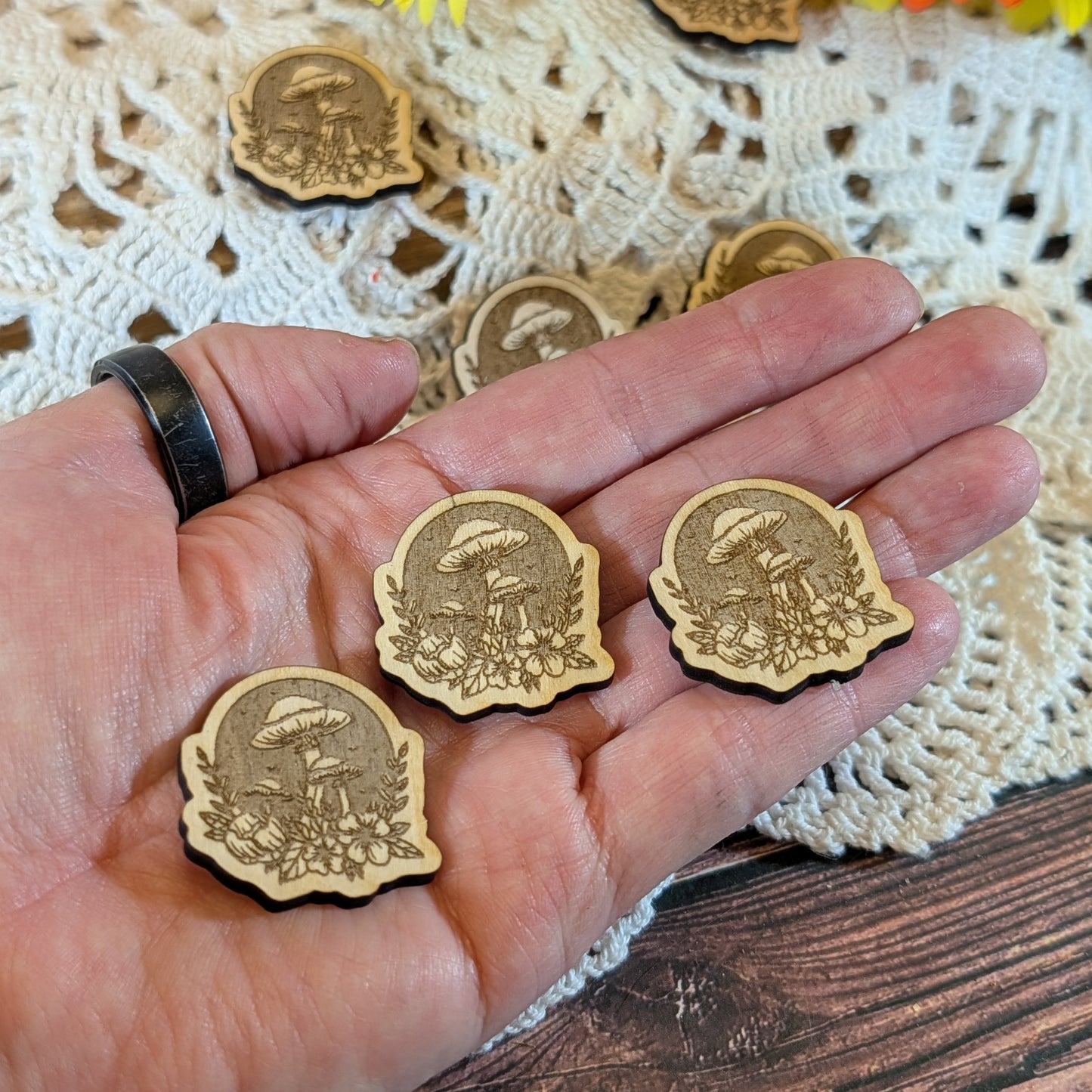Hand holding wooden magnets with designs on a lace doily background