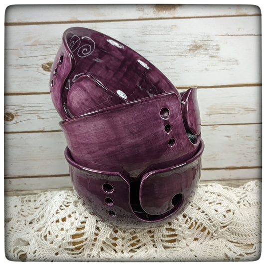 A stack of three purple yarn bowls on a lace doily with a wooden background.